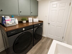 A laundry area with a Samsung washer and dryer, a wooden countertop with detergent bottles, a potted plant, and a sign indicating laundry supplies are provided. - Stylish & Modern 2BR Suite -Private Entry - Prime Location (Atlanta)
