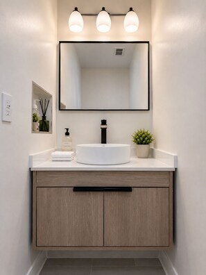 A bathroom with a white sink, a large mirror, and three wall-mounted lights. - Stylish & Modern 2BR Suite -Private Entry - Prime Location (Atlanta)