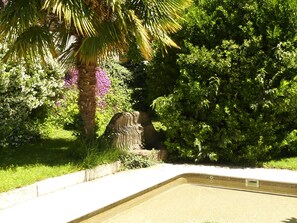 Ein Pool mit einer Steinstruktur, umgeben von üppiger Vegetation und blühenden Pflanzen.