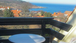 En balkong med ett bord och stolar, med utsikt över en kuststad med hus och havet.
