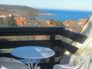 A balcony with a table and chairs, overlooking a coastal town with houses and the sea. - Semi-detached house with sea view in Sandvig (Allinge-Sandvig)