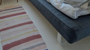 Ett sovrum med en säng, ett fönster med utsikt, en hylla med böcker och en inramad tavla samt ett litet bord med handdukar.
