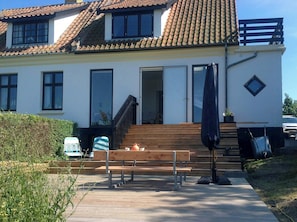 Ein zweistöckiges Haus mit Ziegeldach, einer Veranda mit Holzstufen und einer Bank.