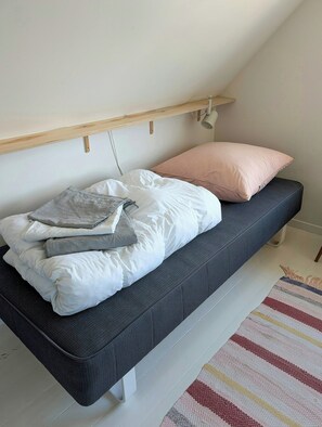Un lit avec un matelas foncé, des oreillers blancs et une couverture pliée.