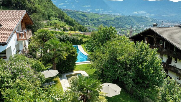 Un barrio residencial con piscina, abundante vegetación y montañas al fondo.