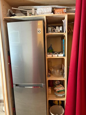 Eine kompakte Küche mit einem Edelstahlkühlschrank, Holzregalen und einem roten Vorhang.