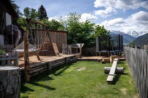 Ein rustikaler Spielbereich im Freien mit Holzkonstruktionen, einer Schaukel und Blick auf Berge.