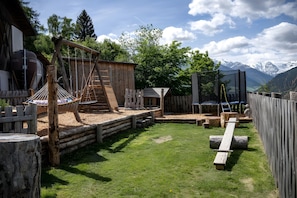 Ein rustikaler Spielbereich im Freien mit Holzkonstruktionen, einer Schaukel und Blick auf Berge.