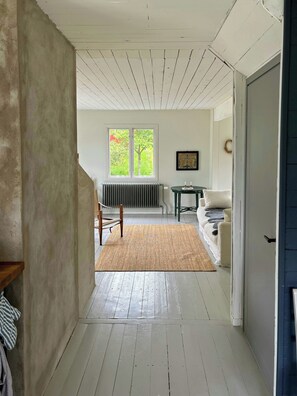 Ein Flur mit Heizkörper, einem Fenster mit Blick auf Bäume, einem gerahmten Bild an der Wand und einer Tür rechts.