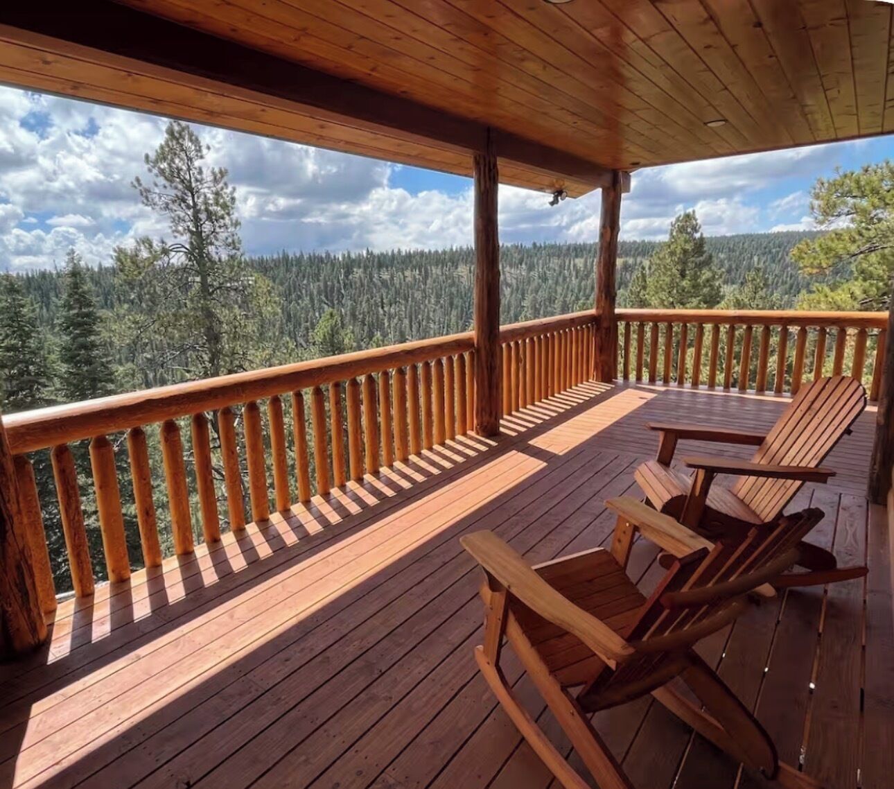 Eine Holzterrasse mit Geländer, zwei Adirondack-Stühle und Blick auf einen bewaldeten Gebirgszug.