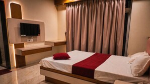 A modern hotel room with a bed, a TV mounted on the wall, and a large window with curtains. - Hotel krushna palace lodge  (Wadwani)
