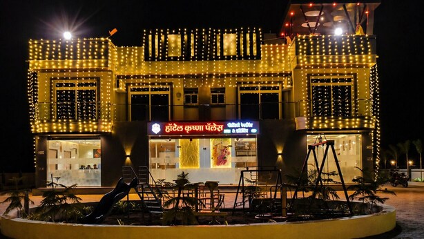 A hotel with a well-lit facade, a central entrance, and a seating area with tables and chairs. - Hotel krushna palace lodge  (Wadwani)