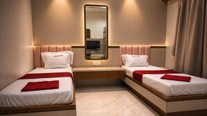 A hotel room with two beds, a mirror, a TV, and a small seating area. - Hotel krushna palace lodge  (Wadwani)