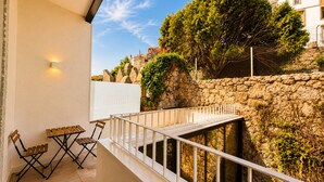 Ein Balkon mit einer Steinmauer, einem weißen Geländer und Blick auf einen Baum und Gebäude.