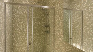 Ein Badezimmer mit Duschkabine aus Glas, einem Waschbecken inklusive Spiegel und einem runden Dachfenster.