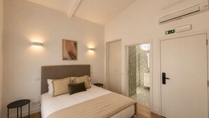 Ein Schlafzimmer mit Bett, Nachttischen, einer Wand-Klimaanlage und einer Tür zu einem Badezimmer.