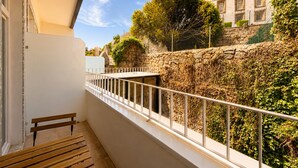 Ein Balkon mit einer hölzernen Bank, einer Steinmauer und Blick auf Gebäude und Bäume.