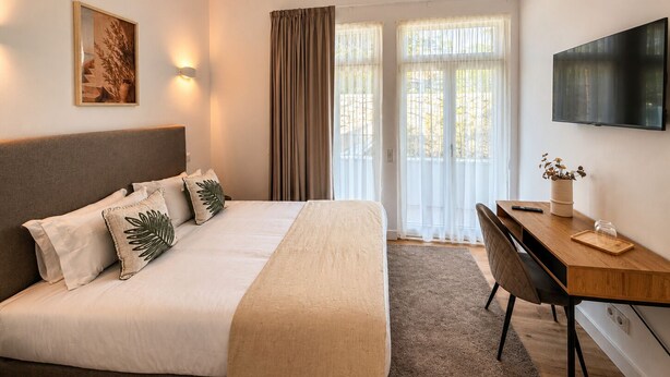 Ein Hotelzimmer mit Bett, Schreibtisch, Fernseher und einem Fenster mit Vorhängen.