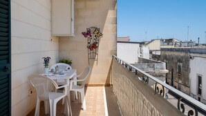 Un balcó amb taula i cadires, una planta en test i un element decoratiu metàl·lic.