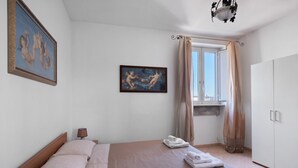 Habitació d'hotel amb un llit, una tauleta de nit, una làmpada, un quadre, una finestra amb cortines i un armari.