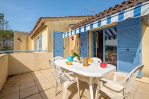 A patio with a white table and chairs, a tiled floor, and a building with blue shutters. - Dream Vacations on the French Riviera: Apartment No. 2 (35 m²) + Private South-Facing Sun Deck (16 m²) (Châteauneuf-Grasse)