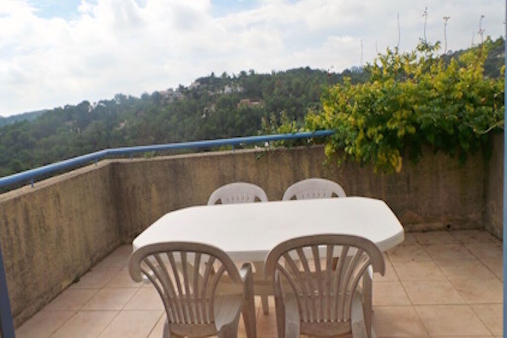 A balcony with a table and chairs, overlooking a hillside.
