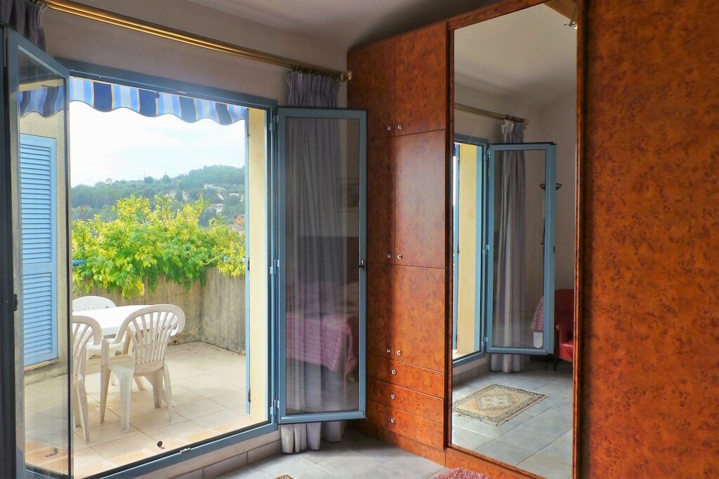 A room with a sliding glass door leading to a patio with a table and chairs, a mirrored wardrobe, and a tiled floor.