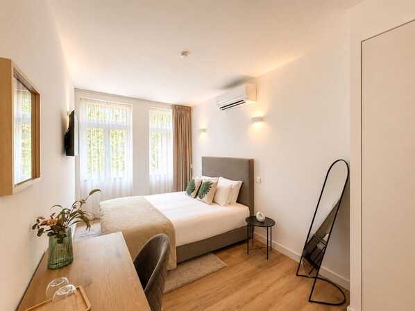 Ein Hotelzimmer mit Bett, Schreibtisch, Stuhl, einem kleinen Tisch, einem Spiegel und einer Zimmerpflanze.