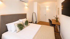 Une chambre d’hôtel comprenant un lit, une table de chevet, une chaise, un bureau, un appareil de climatisation et une porte.