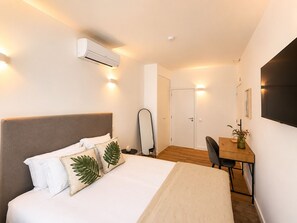 Ein Hotelzimmer mit Bett, Nachttisch, Stuhl, Schreibtisch, Klimaanlage und einer Tür.