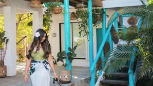 A woman walking a dog on a concrete path with a wooden bridge and a thatched-roof building in the background. - July10th Hotel By Punta Rucia (Punta Rucia)