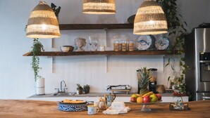 A kitchen with wooden shelves, hanging wicker lights, a fruit bowl, and a coffee maker. - July10th Hotel By Punta Rucia (Punta Rucia)
