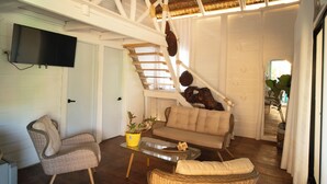 Un amplio salón con techo alto, una escalera, un sofá y un televisor montado en la pared.