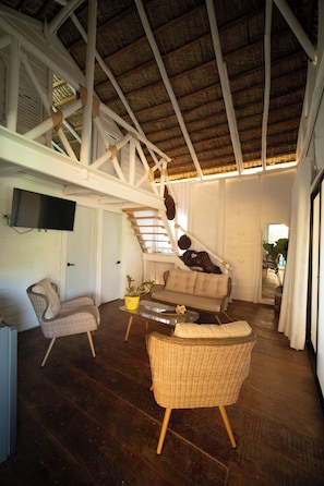 A spacious living area with a high ceiling, a staircase, a sofa, and a television mounted on the wall.