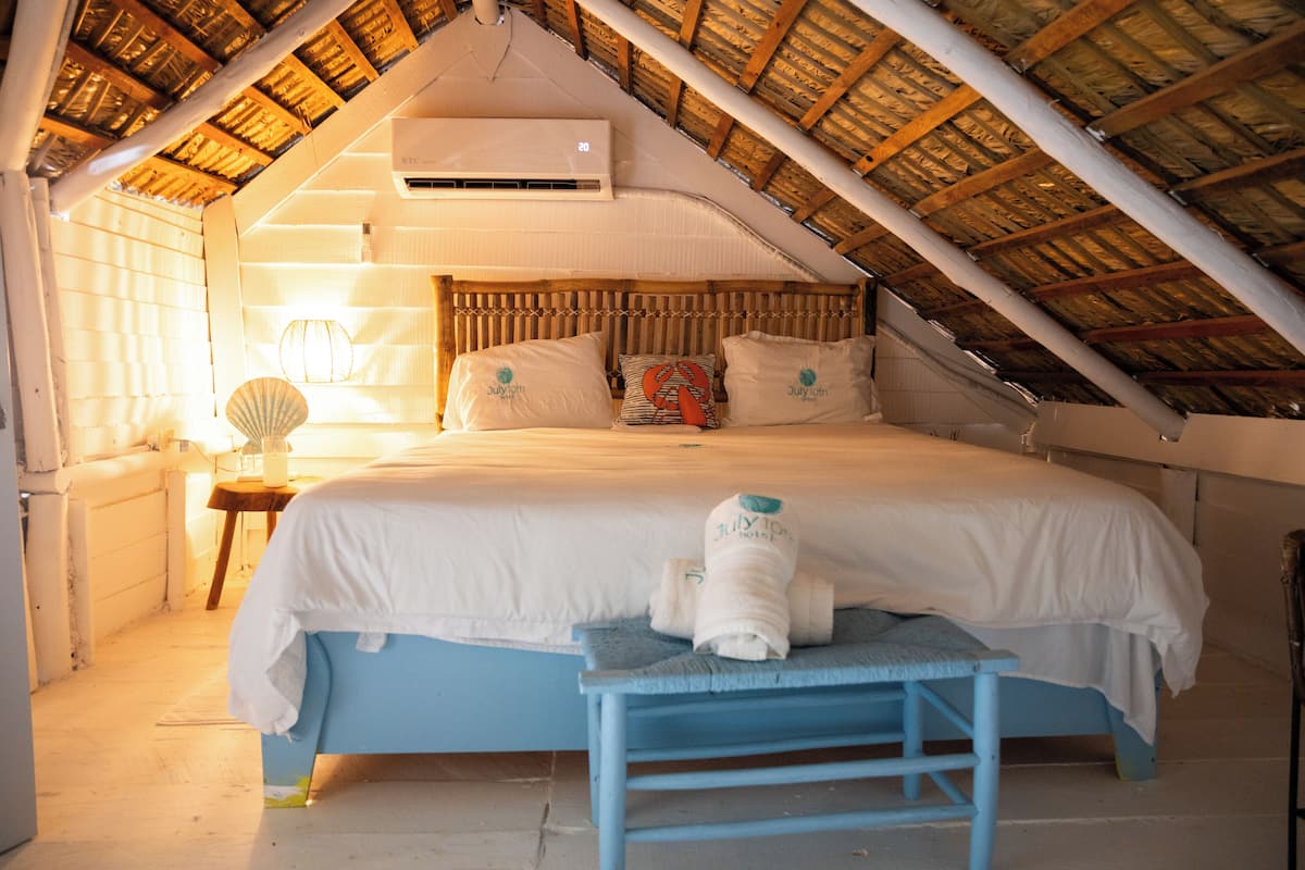 Een slaapkamer met schuine wanden, een bed met witte beddengoed, een bedlamp en een handdoek op de bank.