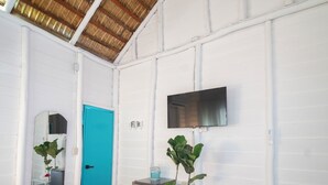 A bedroom with a bed, a blue door, a TV on the wall, a small table, and a plant. - July10th Hotel By Punta Rucia (Punta Rucia)