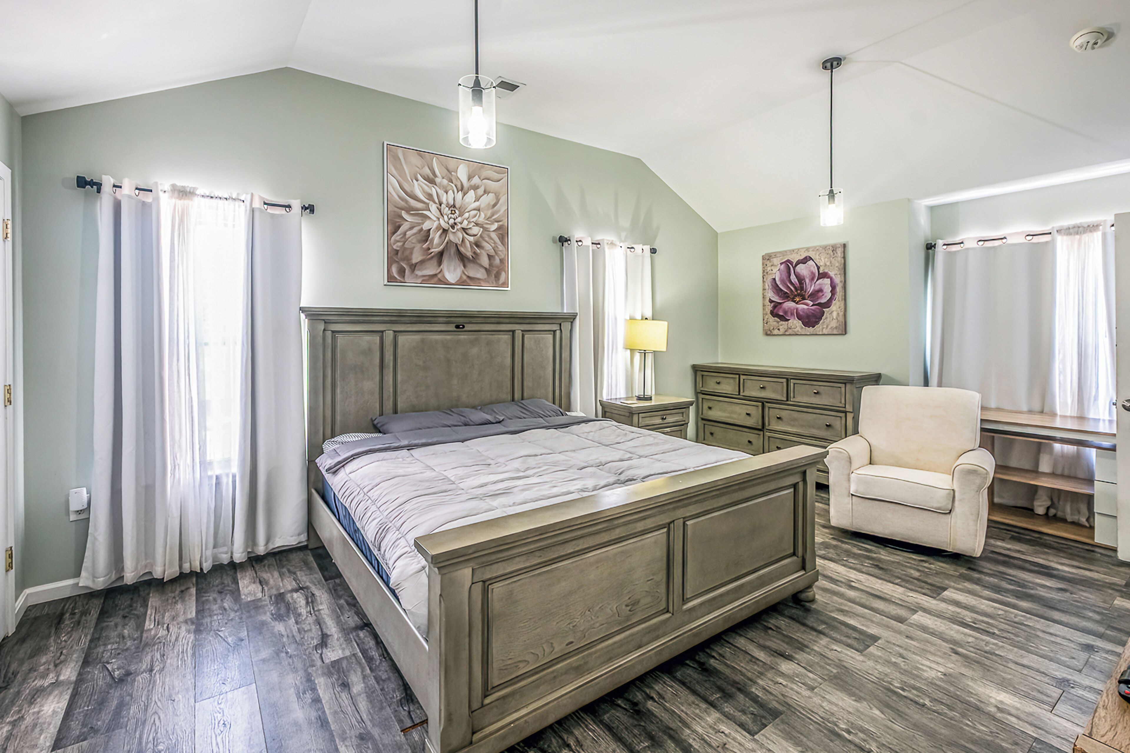 Un dormitorio con cama, una silla, un escritorio y obras de arte en las paredes.
