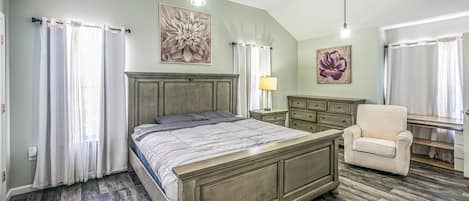 Un dormitorio con cama, una silla, un escritorio y obras de arte en las paredes.