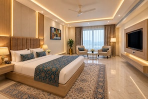 Habitación de hotel moderna con una cama grande, un televisor de pantalla plana, una zona de estar con dos sillones y un ventanal con cortinas.