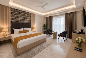 A modern hotel room with a large bed, a desk with a TV, a seating area, and a ceiling fan.