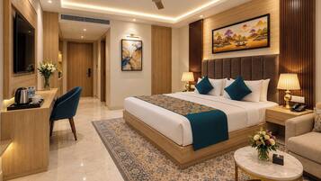 A hotel room with a large bed, a desk with a chair, a sofa, a small round table, and a painting on the wall.