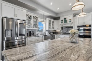 A modern kitchen with stainless steel appliances, white cabinetry, and a marble countertop. - Serenade by the Sea! Coastal Escape, Private Pool, Gulf Views (Panama City Beach)