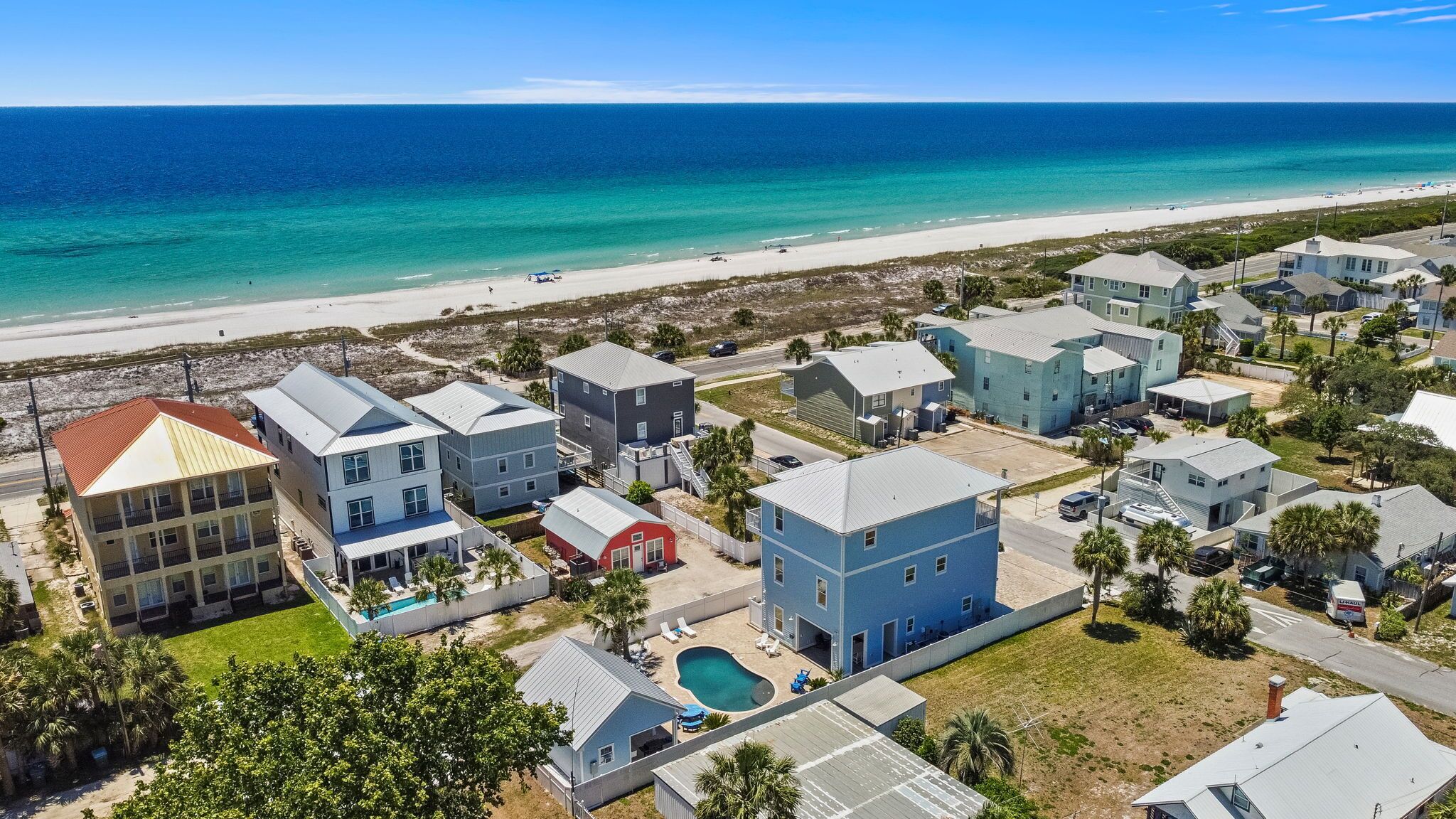 A coastal residential area with multiple two-story houses, a swimming pool, and a beach in the background.