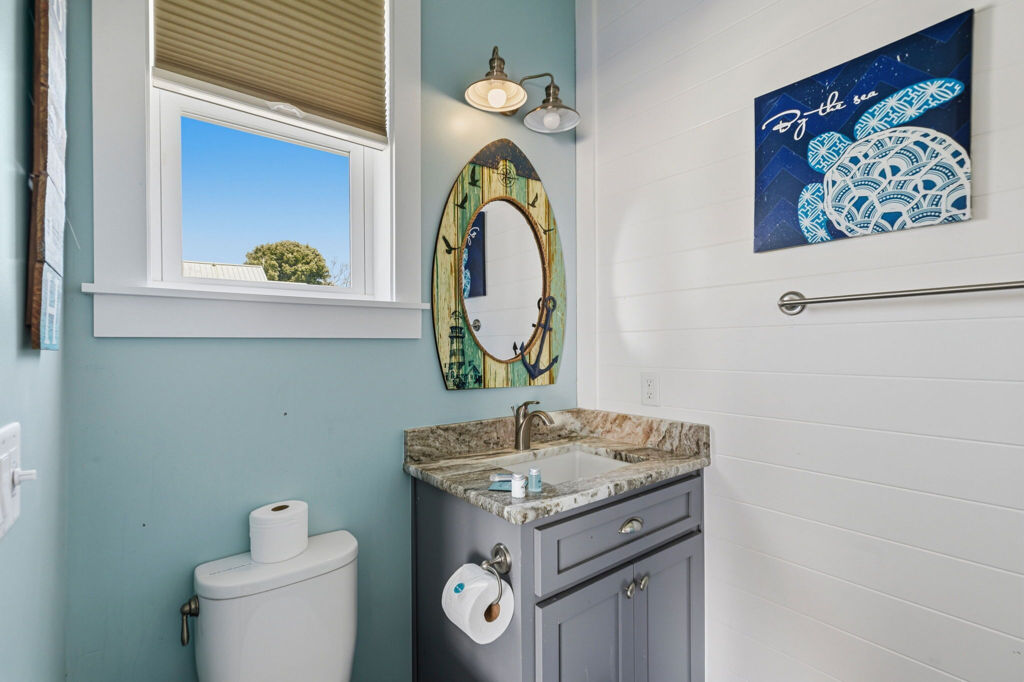 A bathroom with a toilet, sink, vanity, mirror, and a window with blinds.