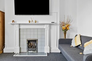 Ein Wohnzimmer mit Kamin, einem grauen Sofa und einem Flachbildfernseher, der über dem Kamin angebracht ist.