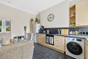 Eine kompakte Küche mit Waschmaschine, Mikrowelle und einer Uhr an der Wand.