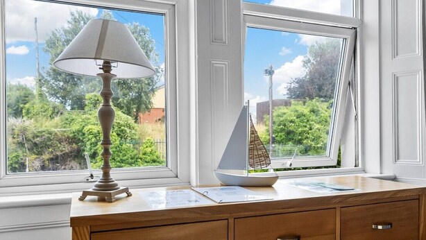 A wooden dresser with drawers, a lamp, and a model sailboat on a windowsill. - Spacious sea view apartment, West Hoe Free Parking (Plymouth)
