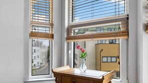 A corner room with a wooden desk, a vase with flowers, and a window with blinds. - Spacious sea view apartment, West Hoe Free Parking (Plymouth)