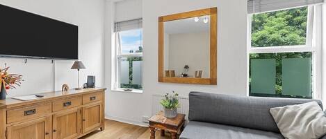 Una sala de estar moderna con un televisor de pantalla plana, un mueble de madera, un sofá gris y un espejo grande.