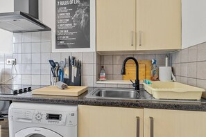 Eine Küche mit einem Poster, einer Spüle, einem Geschirrgestell, einer Waschmaschine und Schränken.